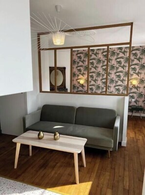 A modern living room with a grey sofa, a wooden coffee table, and a decorative wall panel with a palm tree pattern. - La Verrière ISAHORA - Bright apartment in the heart of the royal city of Eu (Eu)