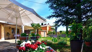 A garden with potted plants and flowers, a white umbrella, and a building with a stone facade. - Wonderful terrace retreat (Savudrija)