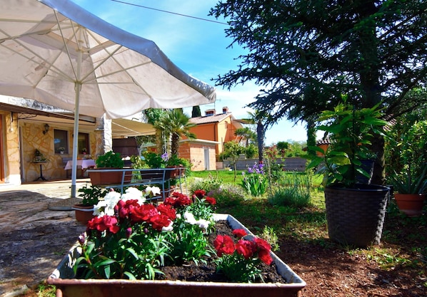 A garden with potted plants and flowers, a white umbrella, and a building with a stone facade.