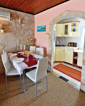 A dining area with a stone wall, a kitchen with yellow cabinets, and a red rug leading to the entrance.