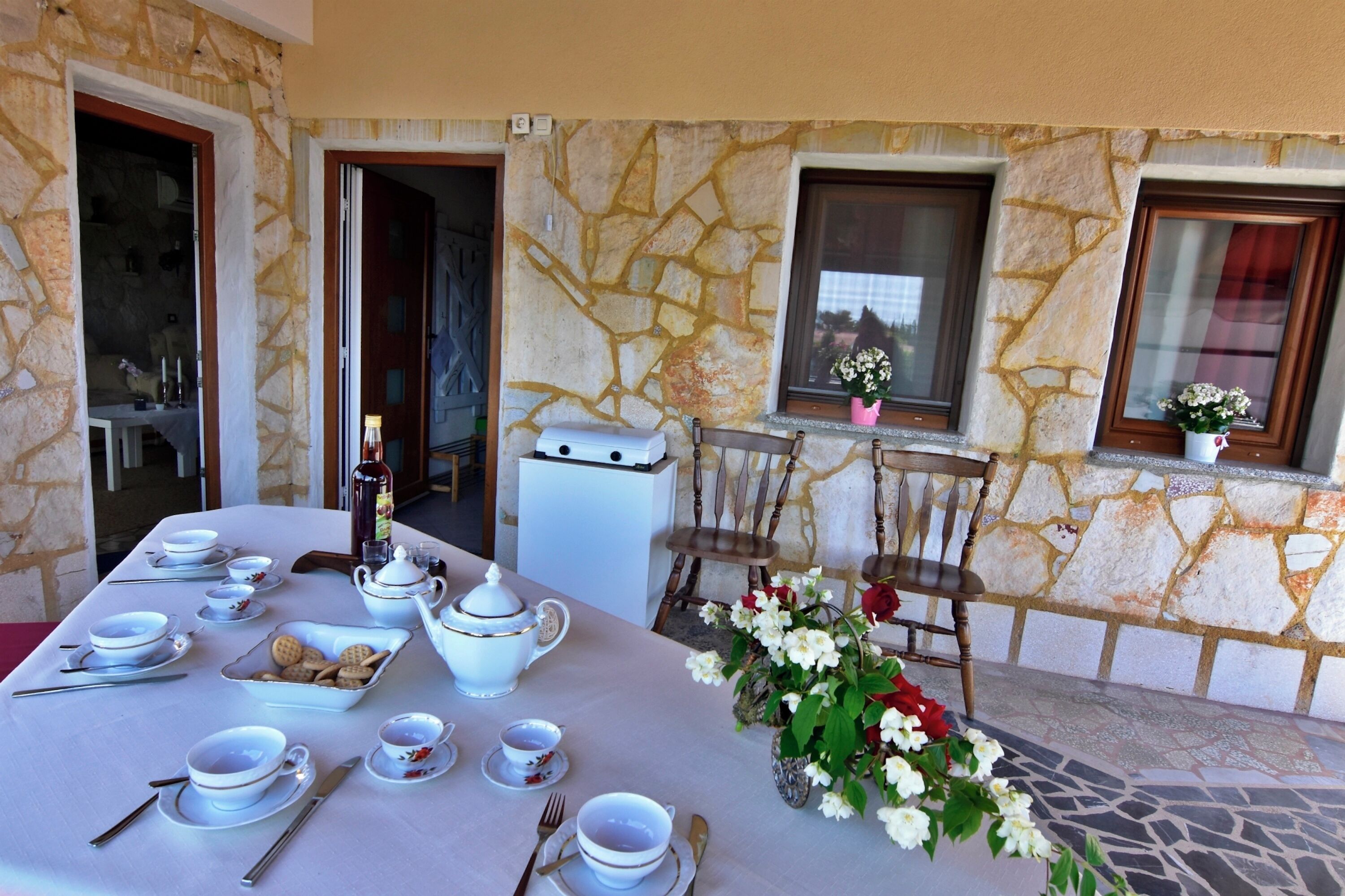 A dining table set with white tableware, a vase with flowers, and a stone wall backdrop.