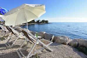 A beachside setting with lounge chairs, a table with a bottle, and a large umbrella.