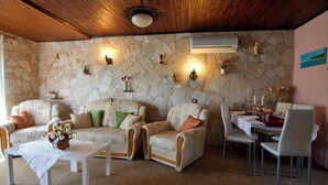 A room with a stone wall, a wooden ceiling, a sofa set, a dining table with chairs, and a small table with a vase of flowers. - Wonderful terrace retreat (Savudrija)