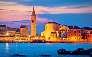 A coastal town at dusk with a prominent tower and stone buildings. - Peaceful studio in Šćavonija (Murine)