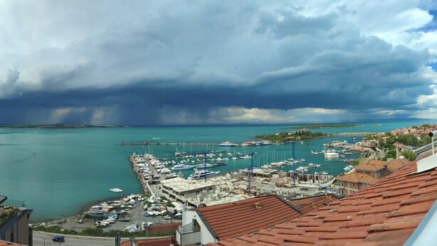 Un port de plaisance sur la côte, avec des bateaux amarrés, un abri et une vue sur la mer sous un ciel nuageux.