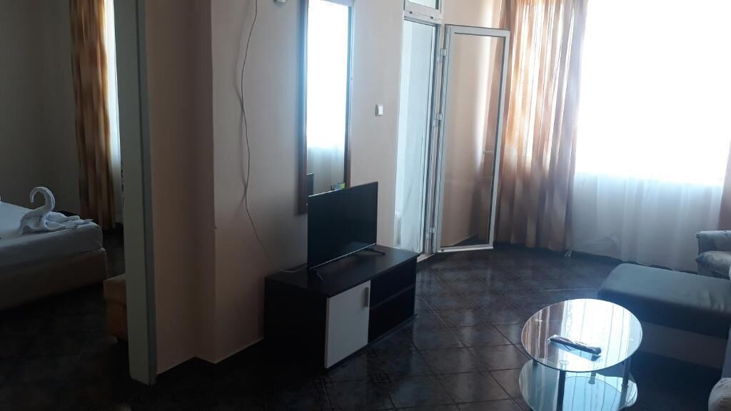 Ein Hotelzimmer mit einer Couch, einem Fernseher auf einem Schrank, einem Glastisch und einer Schiebetür, die auf einen Balkon führt.