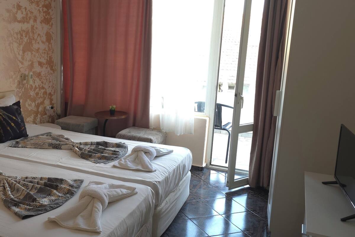 A hotel room with two beds, a small table, a TV, and a view of the outside.