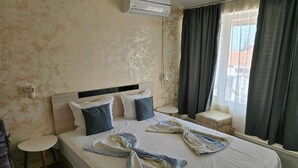 Une chambre d’hôtel avec un lit, une petite table ronde, une chaise, un appareil de climatisation et une vue sur l’extérieur.