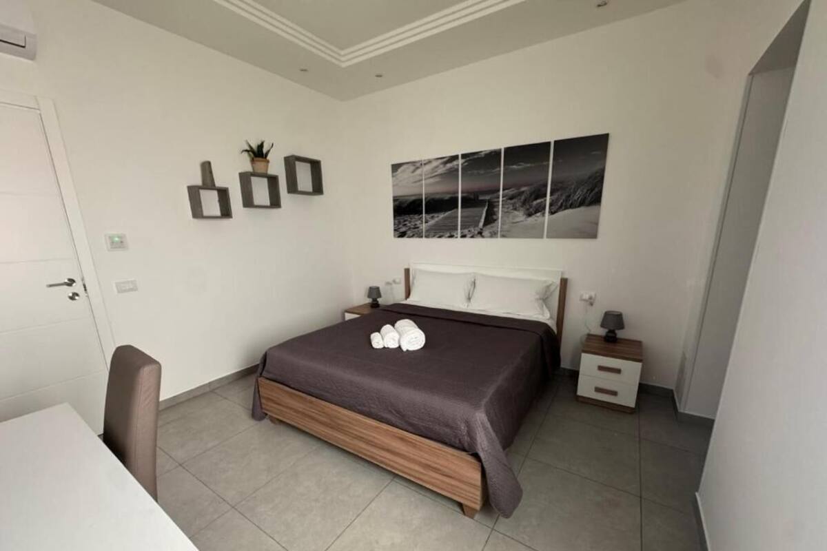 A bedroom with a bed, bedside table, chair, and a wall-mounted artwork.