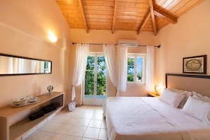 A bedroom with a bed, a bedside table, a mirror, a window with curtains, and a balcony view. - Almondtree House Exanthia - Private Parking (Lefkada)