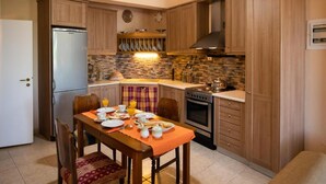 A compact kitchen with wooden cabinets, a built-in oven, and a dining area with a table set for breakfast. - Almondtree House Exanthia - Private Parking (Lefkada)