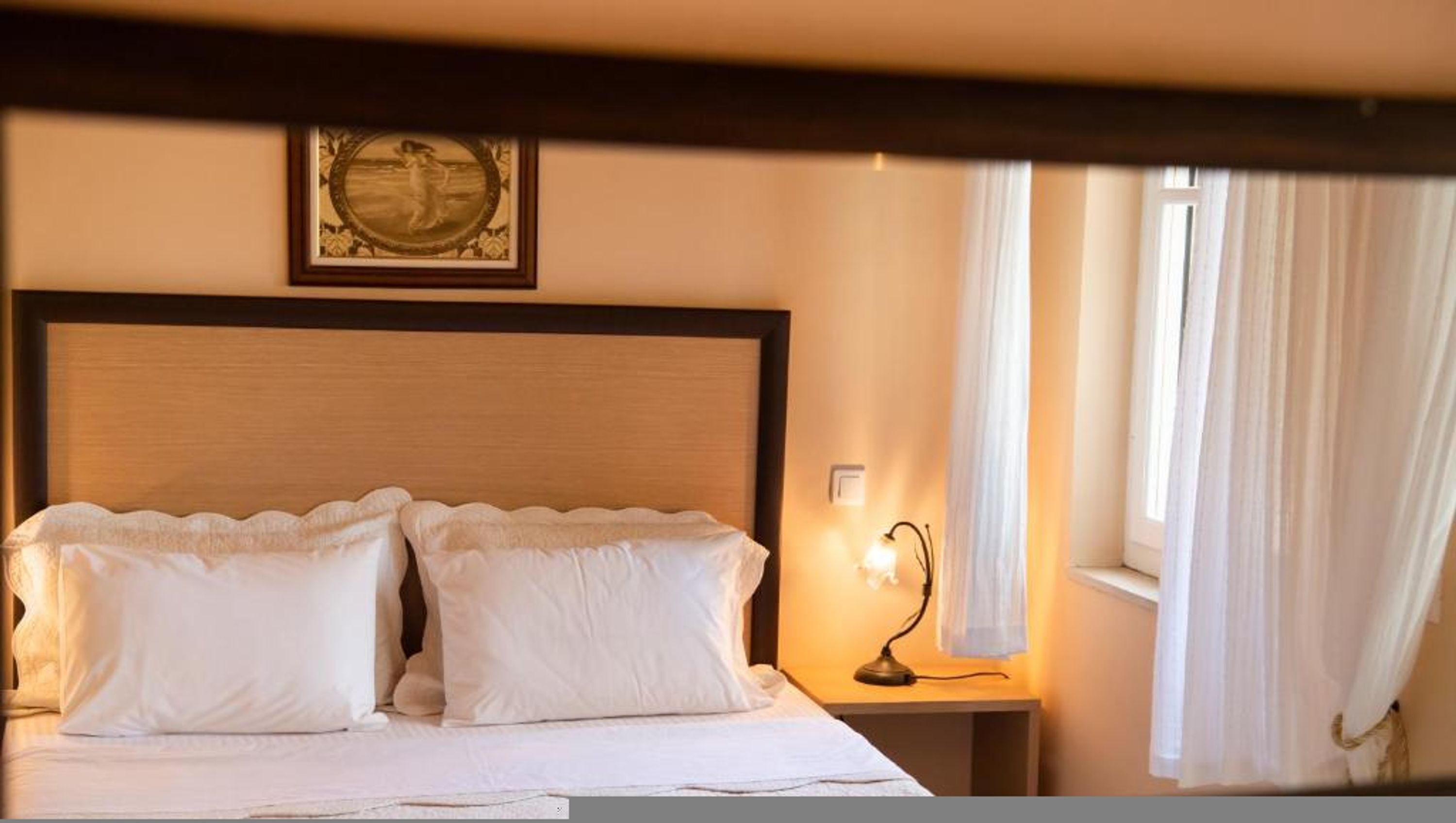 A hotel room with a large bed, a nightstand with a lamp, and a framed picture on the wall.