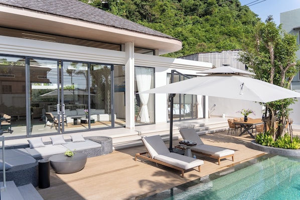 A modern outdoor pool area with lounge chairs, a dining table, and a large umbrella.