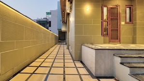 A corridor with tiled flooring, a wooden door, and a small window. - Alaya Stays Freesia 3BHK Apartment (Greater Noida)