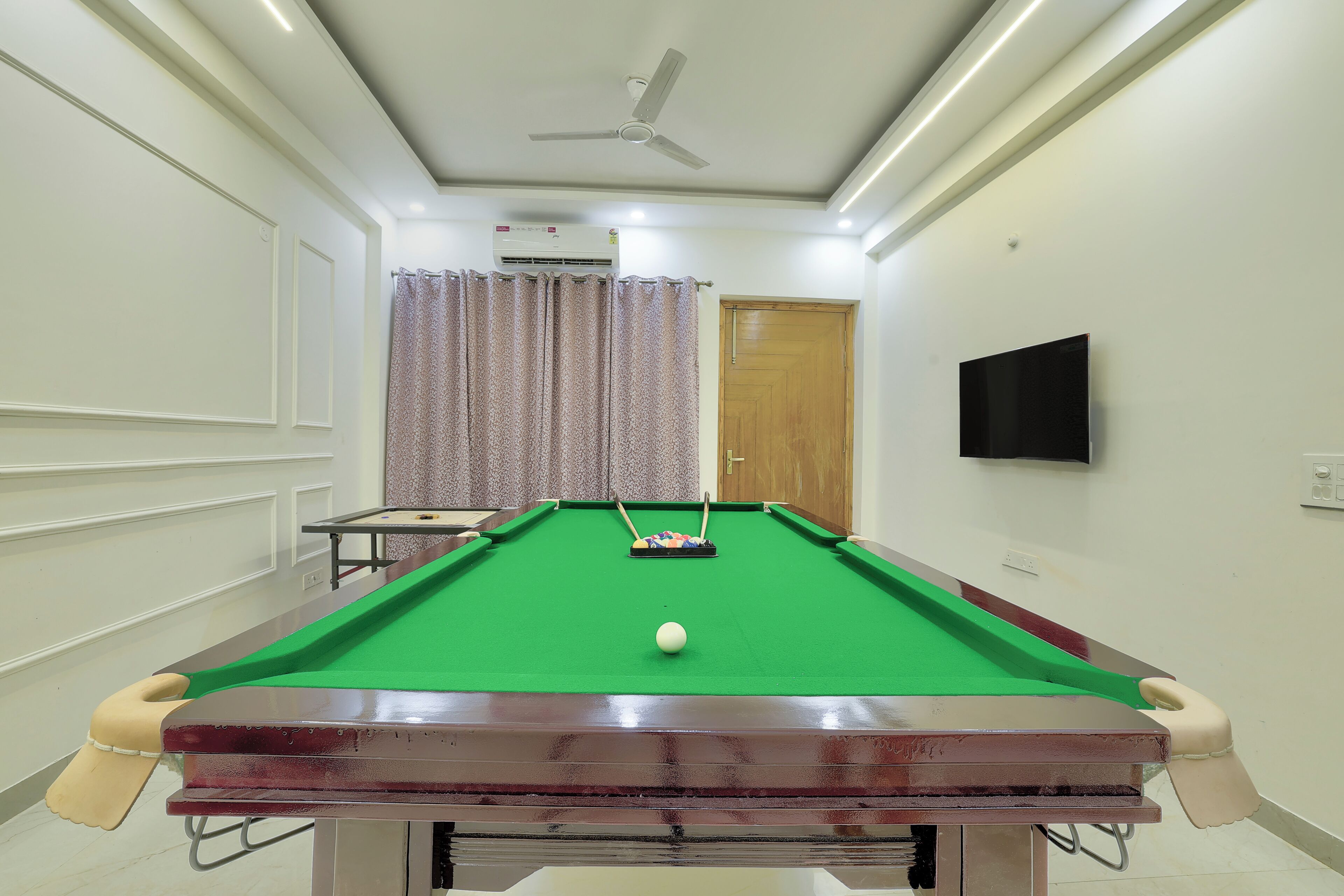 A pool table with a cue ball, a ceiling fan, and a television on the wall.