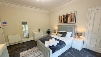 A bedroom with a bed, bedside tables, a mirror, a large windows, and a radiator.