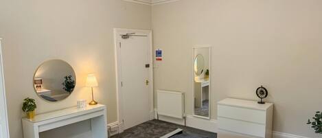 A bedroom with a bed, bedside table, lamp, mirror, a radiator, and a door.