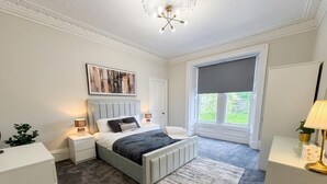A bedroom with a bed, bedside tables, a nightstand, a window with a view, and a chandelier. - Stylish River View Stay Sleeps 6 (Dundee)
