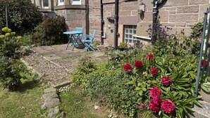 A stone building with a garden, outdoor seating, and a small window. - Stylish River View Stay Sleeps 6 (Dundee)