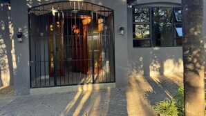 A modern house with a gated entrance, a visible porch, and a window overlooking the yard. - Boutique Hotel-Style 8Bed Villa Ferndale (Randburg)