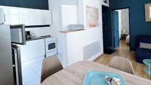 A modern kitchen with white cabinets, a dining table with chairs, and a blue tray on the table. - Le Balcon Notre Dame - 3★ apartment with balcony in the heart of Le Tréport (Le Tréport)
