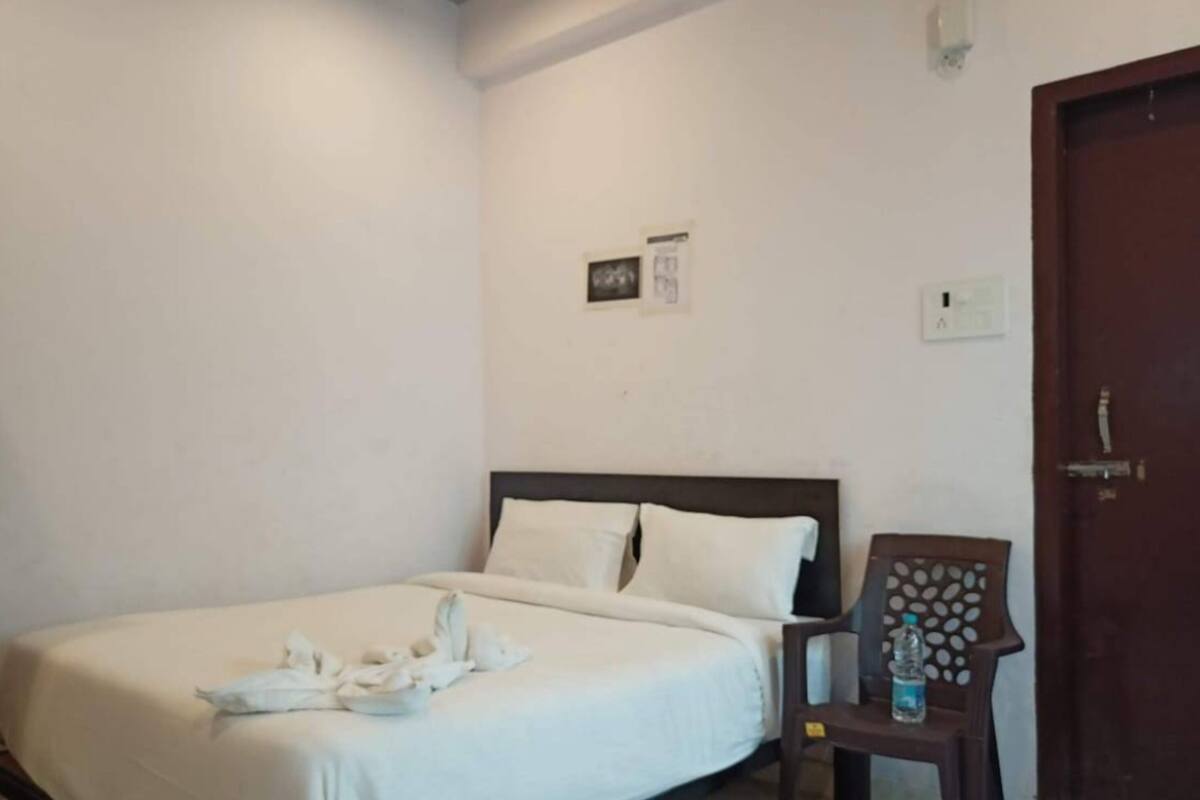 A neatly made bed with white linens and towels, a wooden headboard, a chair with a patterned backrest, and a door with a handle.