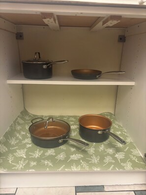 Une cuisine avec deux étagères : sur la première, on trouve une casserole et une poêle, et sur la seconde, deux poêles.