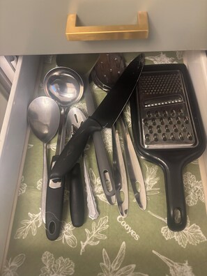 A drawer with various kitchen utensils including a knife, spoon, spatula, and grater. - 1st Floor Spacious Apt with Deck (Kearny)
