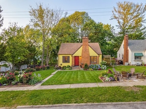 A yellow house with a red door, surrounded by a well-maintained lawn and garden. - Theater Nights, Game Room & Balcony Delights (Rockford)