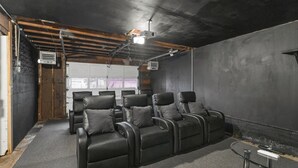 A room with a projector, a white door, and a seating area with black chairs. - Theater Nights, Game Room & Balcony Delights (Rockford)