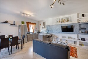 Eine moderne Küche mit Fernseher, Essbereich mit Stühlen und einer Couch.