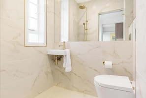 Ein modernes Badezimmer mit Toilette in Weiß, einem Waschbecken mit goldener Armatur, einer Dusche mit goldener Duschbrause und einem großen Spiegel.