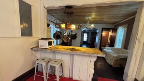 A compact kitchen with a wooden island, white bar stools, hanging pots, and a chandelier. - Long Term- Monthly/Yearly (Bradford)