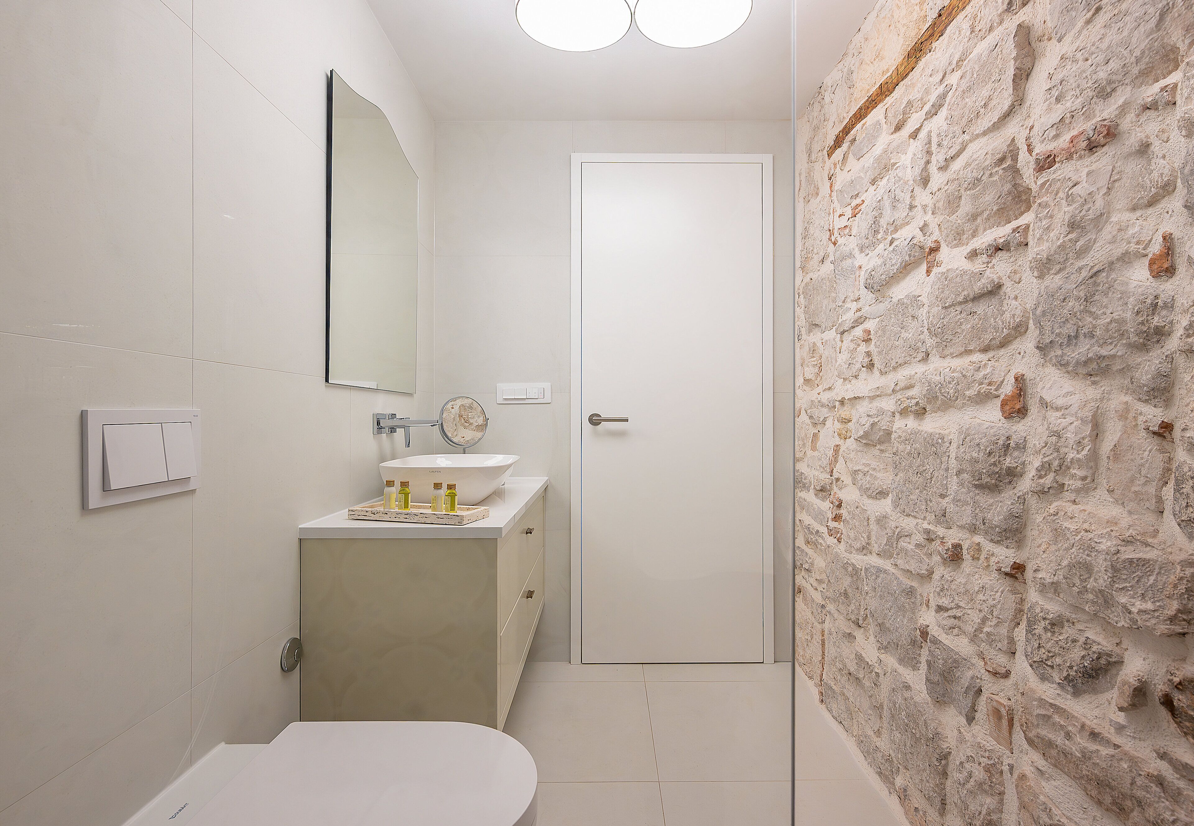 A bathroom with a toilet, sink, mirror, and a door.