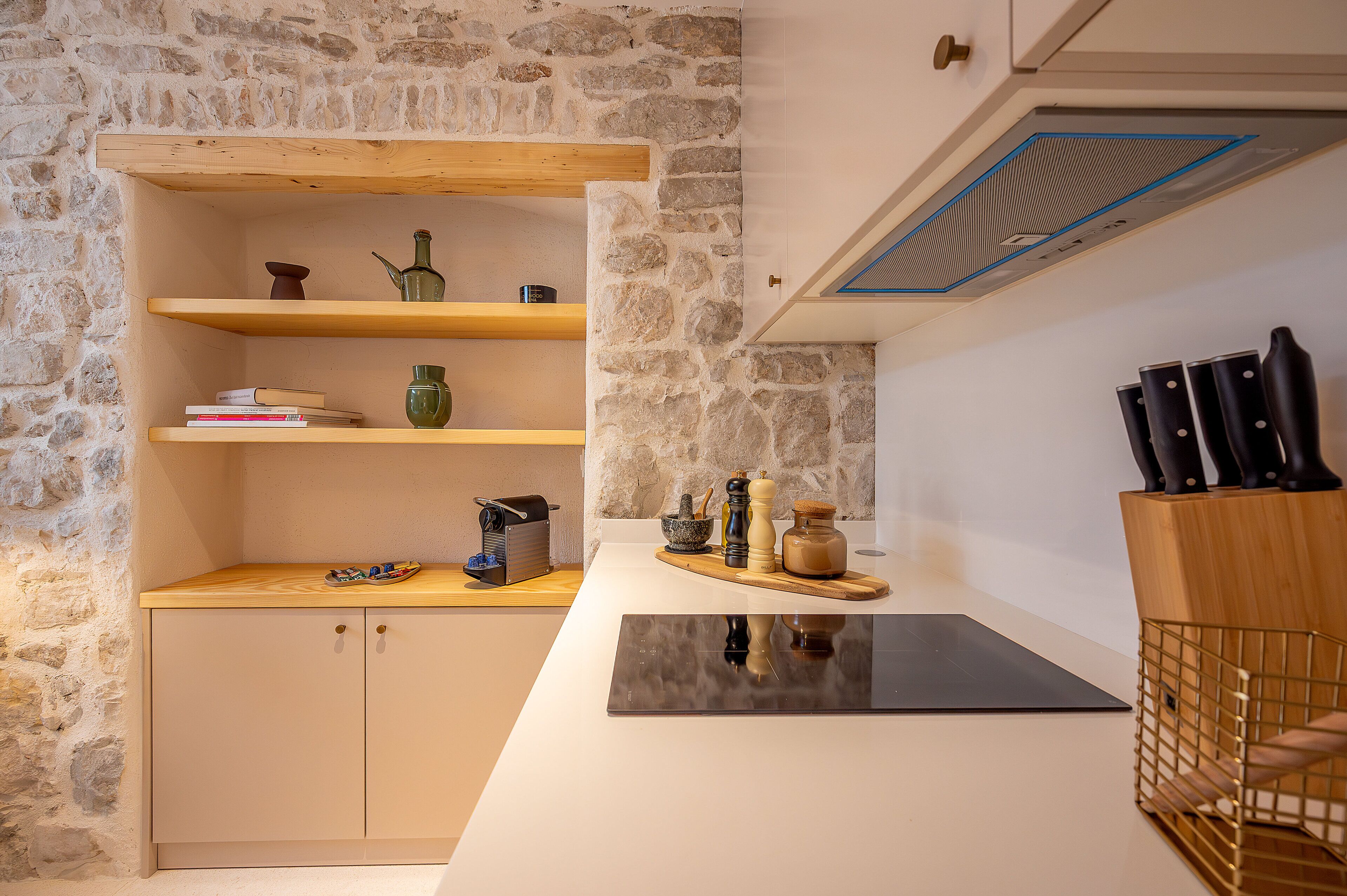 A kitchen with a stone wall, wooden shelves, a black countertop, and a knife block.