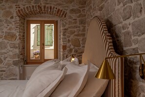 A room with stone walls, a bed with white linens, a window with a view, and a striped headboard. - Heritage Boutique apartment with terrace (Kastel Stari)