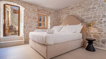Une chambre avec un mur en pierre, un lit recouvert de draps blancs, une petite table et une fenêtre donnant sur un paysage agréable.