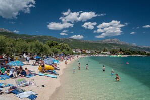 Uma praia com pessoas tomando sol e nadando, cercada por montanhas.