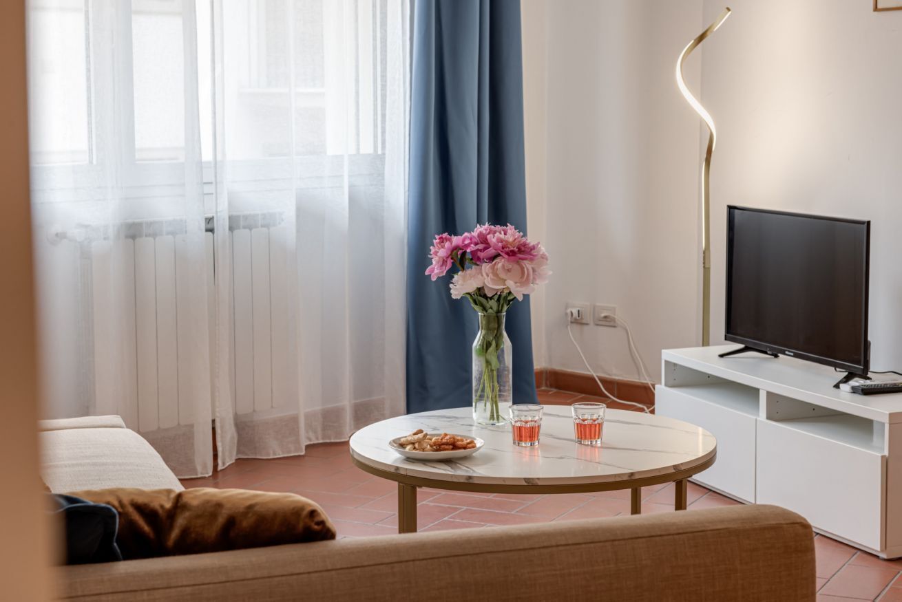 Una sala de estar moderna con una mesa redonda, un televisor de pantalla plana y un jarrón con flores.