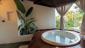 A spa area with a hot tub, wooden flooring, a potted plant, and a view of the garden. - Azorai Hotel Boutique (Santa Cruz Cabrália)