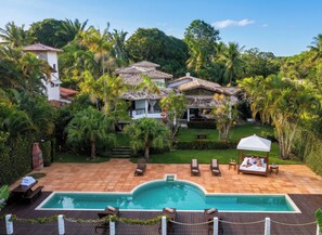 Una villa con piscina, area relax esterna e vegetazione lussureggiante.