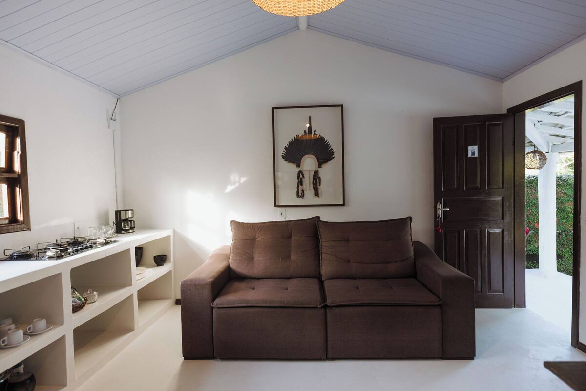 Uma sala de estar com um sofá marrom, prateleiras brancas, um quadro na parede e uma porta que dá para o exterior.