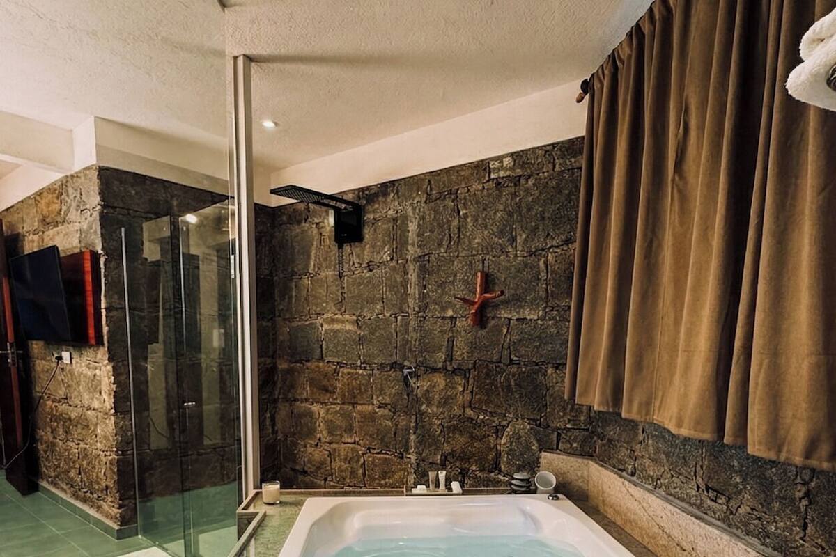 Um quarto de spa com uma banheira grande, paredes de pedra e um box de vidro.