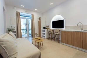 A modern room with a sofa, a small table, a TV, a kitchen area, and a balcony. - Petite Nest - Mikrolimano (Pireas)