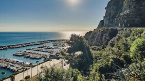 Un port de plaisance sur la côte, avec des bateaux amarrés, un ciel dégagé et une falaise sur laquelle on peut lire le mot « ALASSIO ».