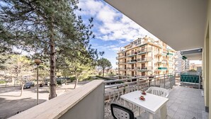 Un balcon avec une table et des chaises, donnant sur un quartier résidentiel avec des immeubles à plusieurs étages et des arbres.