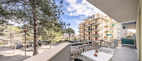 A balcony with a table and chairs, overlooking a residential area with multi-story buildings and trees.