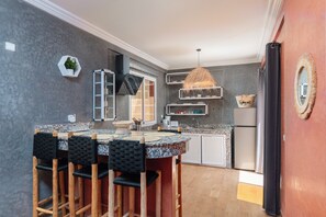 Een keuken met een centraal eiland, barstoelen, een hanglamp en ingebouwde planken.