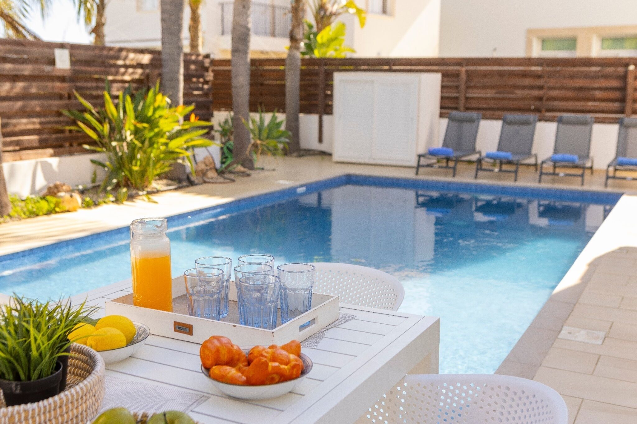 A poolside setting with a table, chairs, a drink, and food.