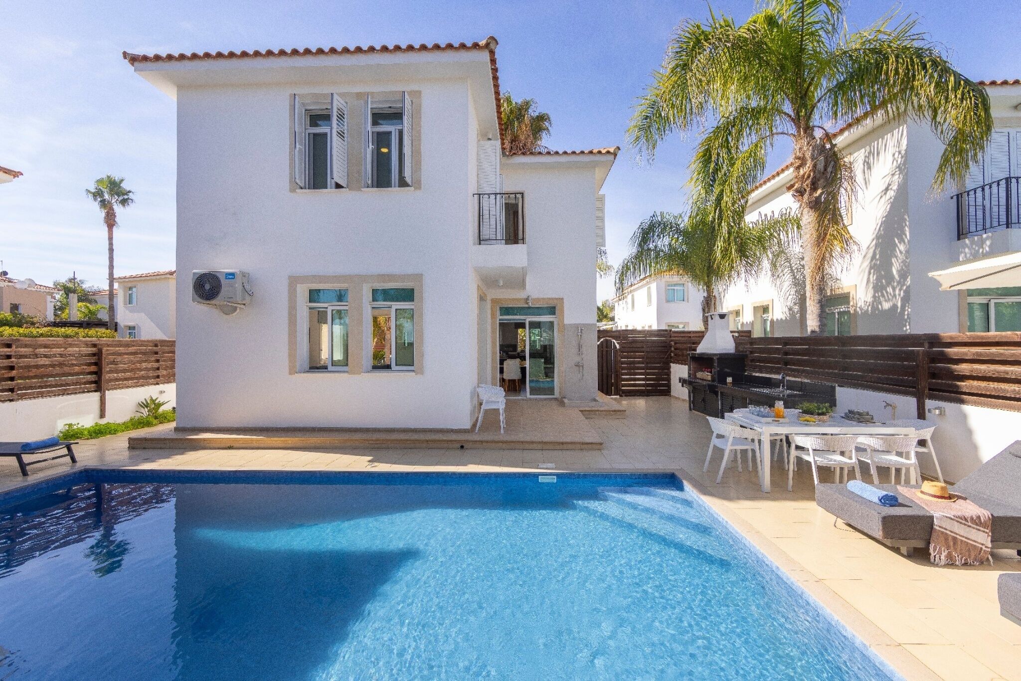 Une maison à deux étages avec une piscine, du mobilier d’extérieur et une clôture en bois.